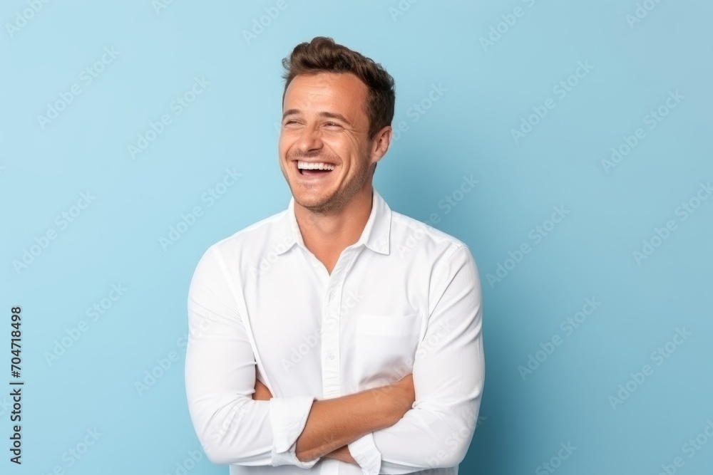 Portrait of a handsome young man laughing with arms crossed on blue background Portrait of a handsome young man laughing with arms crossed on blue background