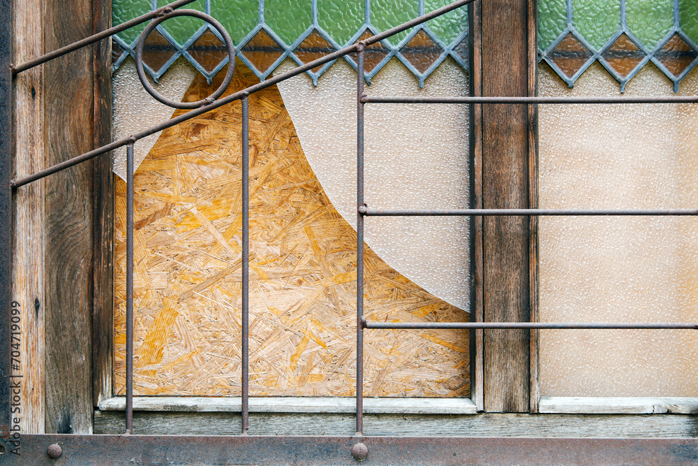 Broken vintage window with iron grilles in the street of Europe. Boarded up window after a break in. The tooth of time or the reflection of war - obrazy, fototapety, plakaty 