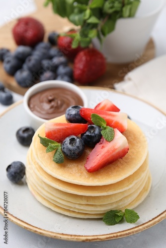 Delicious pancakes with strawberries, blueberries and chocolate sauce on table, closeup