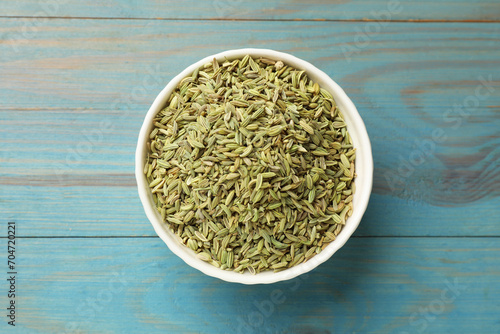 Fennel seeds in bowl on light blue wooden table, top view