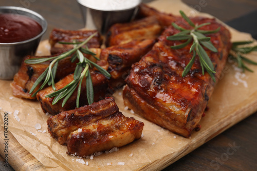 Tasty roasted pork ribs served with sauce and rosemary on wooden table, closeup