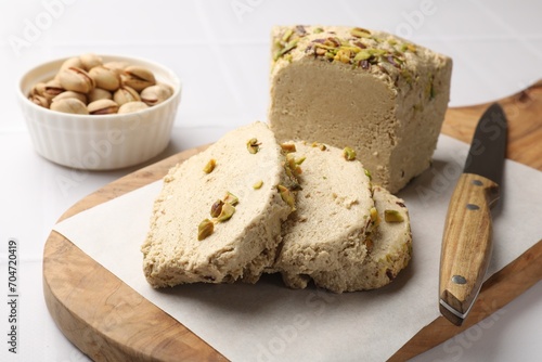 Tasty halva with pistachios and knife on white table, closeup