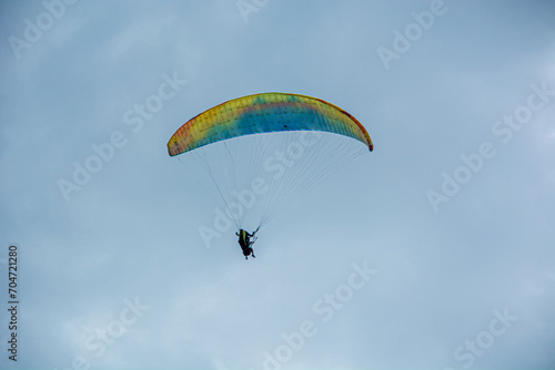 A person paragliding in the sky with a colorful parachute and safety harness.Mountains, Extreme sports in a cloudy day 