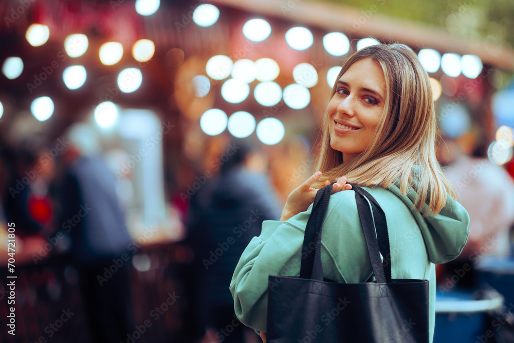Happy Woman Holding a Shopping Bag at a Festive Fair. Cheerful millennial girl getting a bargain in a street market 
 - obrazy, fototapety, plakaty 