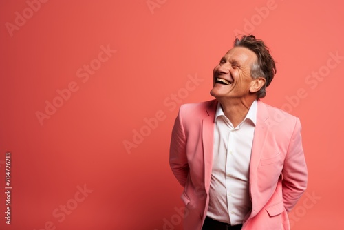 Happy mature man in pink suit laughing and looking at camera on red background