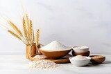 Grains of wheat and different types of flour in a wooden bowl on a white concrete surface.