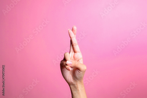 Hand with crossed fingers for luck, isolated on pink background. Hand gesture photo