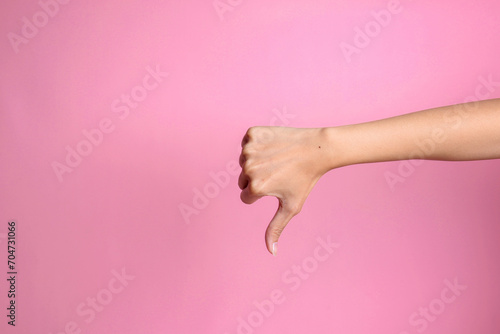 Woman hand showing thumb down sign on pink background. Negative emotions, feelings and signs. photo
