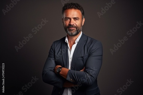 Portrait of a confident mature businessman with arms crossed over dark background. © Chacmool