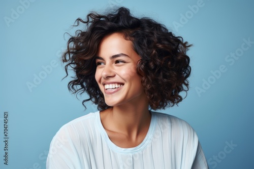Smiling young woman with curly hair on blue background. Closeup portrait