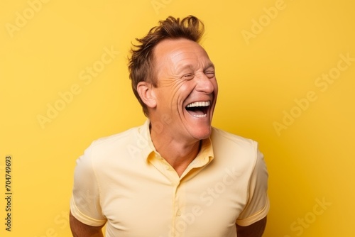 Portrait of a happy mature man laughing and looking up over yellow background