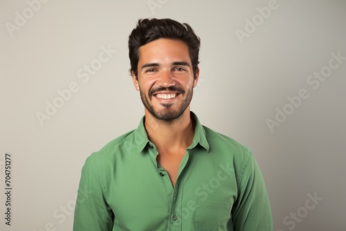 Handsome young man in green shirt smiling and looking at camera on grey background © Inigo
