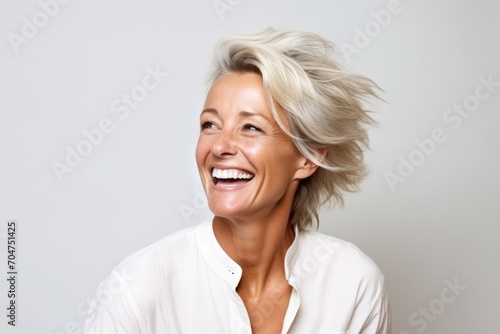 Portrait of happy senior woman with short blonde hair on grey background