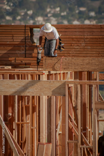 Construction worker on wood framing wearing a white hard hat