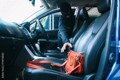 A thief in a robbery mask stealing a purse bag in a car photo