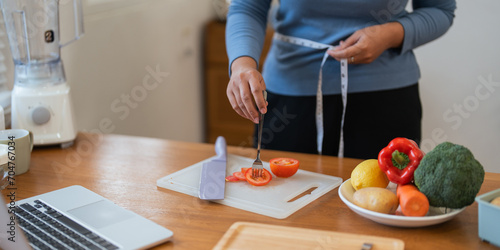 Young woman asian measure her waist in the kitchen the with vegetables and fruits. Concept of healthy eating and dieting