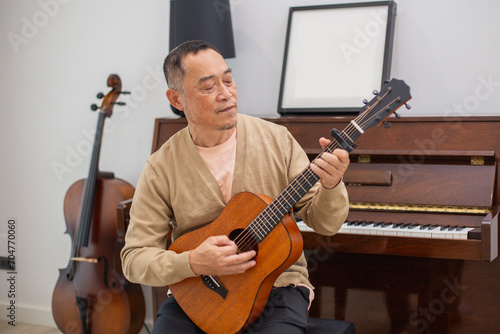Happy asian man senior elderly take it easy on retirement holidays playing guitar having fun in living room at home, Happiness grandfather enjoying singing.