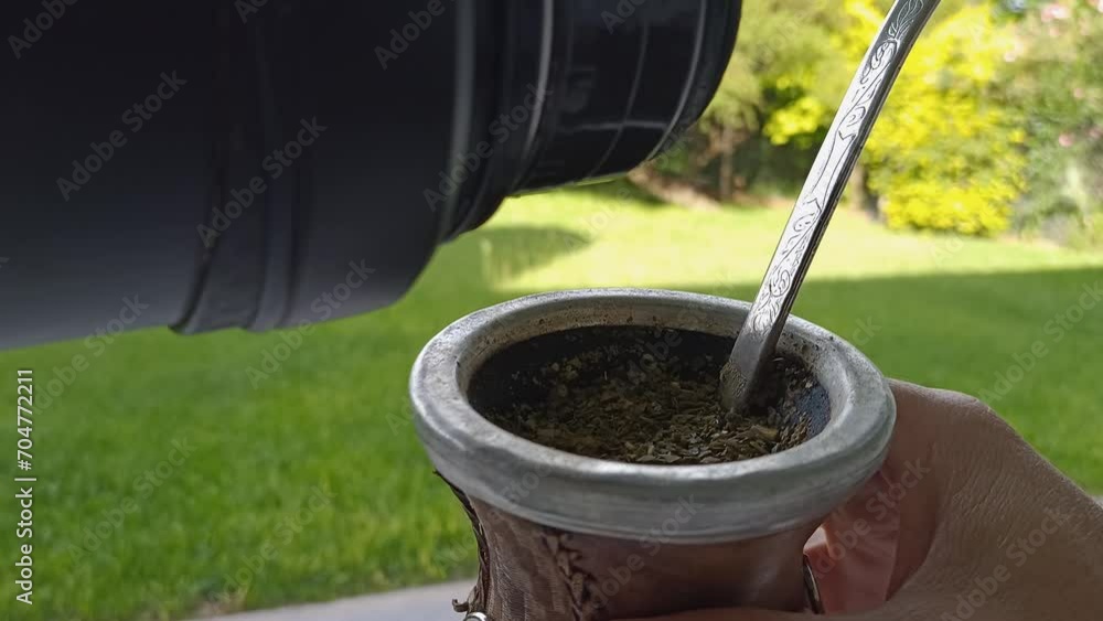 Pouring hot water from thermos into Mate while holding it in hand, traditional drink from Argentina, close up Pouring hot water from thermos into Mate while holding it in hand, traditional drink from Argentina, close up