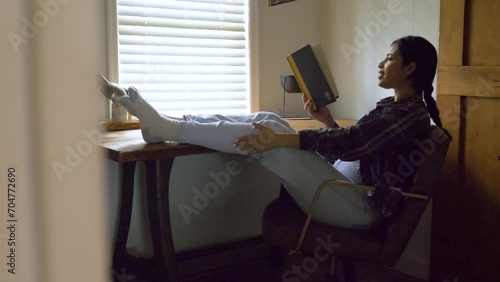 Comfortable Puerto Rican female reading inspirational story book with feet raised resting on desk photo
