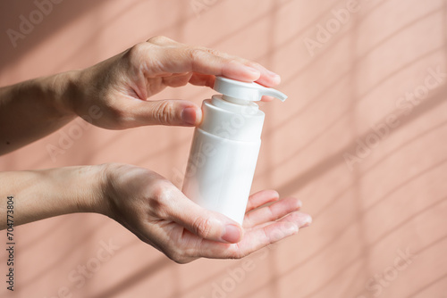 Woman holding a cosmetic bottle with pump on the natural background. Beauty and skin care concept. White pump bottle mock up for branding.
