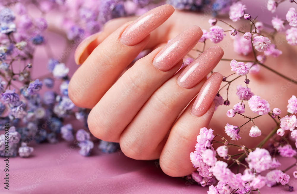 Fototapeta premium Female hands with pink nail design hold gypsophila flowers.