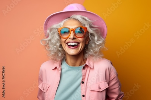 Portrait of a happy senior woman in hat and sunglasses over orange background © Inigo