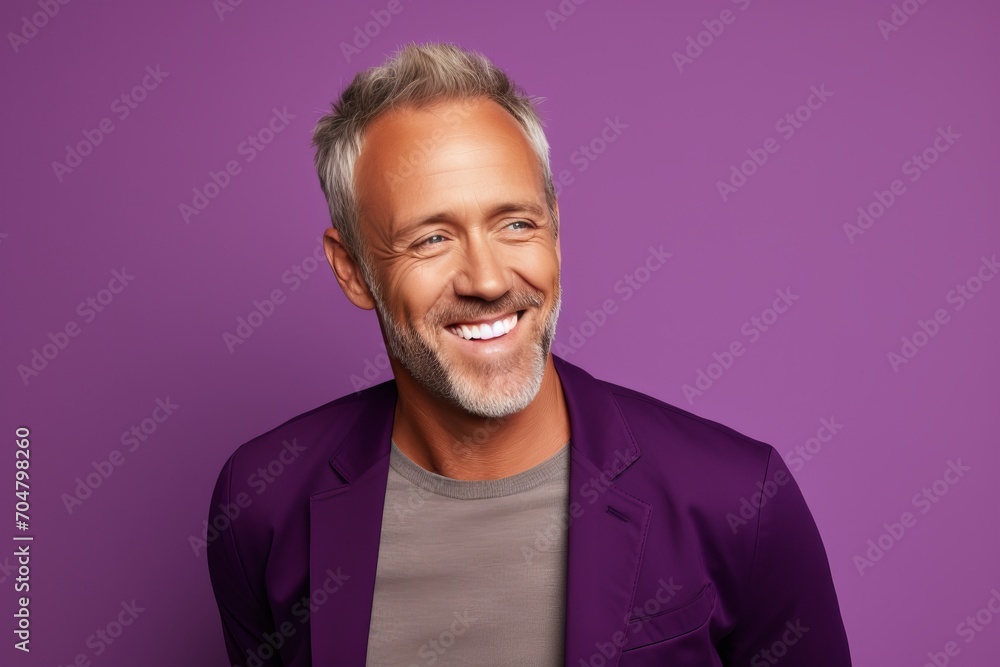Handsome middle-aged man looking at camera and smiling while standing against purple background Handsome middle-aged man looking at camera and smiling while standing against purple background
