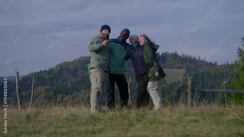 Happy multiethnic friends or hiking buddies take selfie on phone in front of beautiful scenery standing on the top of the hill. Group of diverse tourists during trip in mountains. Outdoor activities. Happy multiethnic friends or hiking buddies take selfie on phone in front of beautiful scenery standing on the top of the hill. Group of diverse tourists during trip in mountains. Outdoor activities.