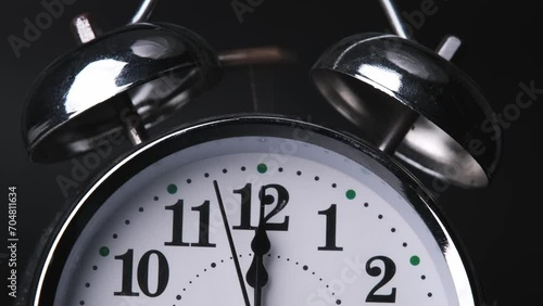 The old alarm clock was ringing at 12:00 AM or 12:00 PM. Close-up of a retro alarm clock face in time lapse on black background. Clock hands move fast.