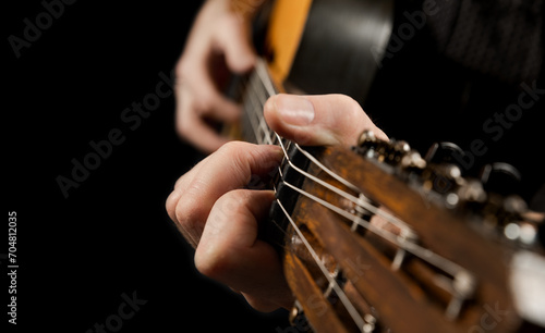 Playing an acoustic guitar on a black background. The musician clamps the frets of the guitar on the neck. Musical instrument in male hands. Close-up. Soft focus.
