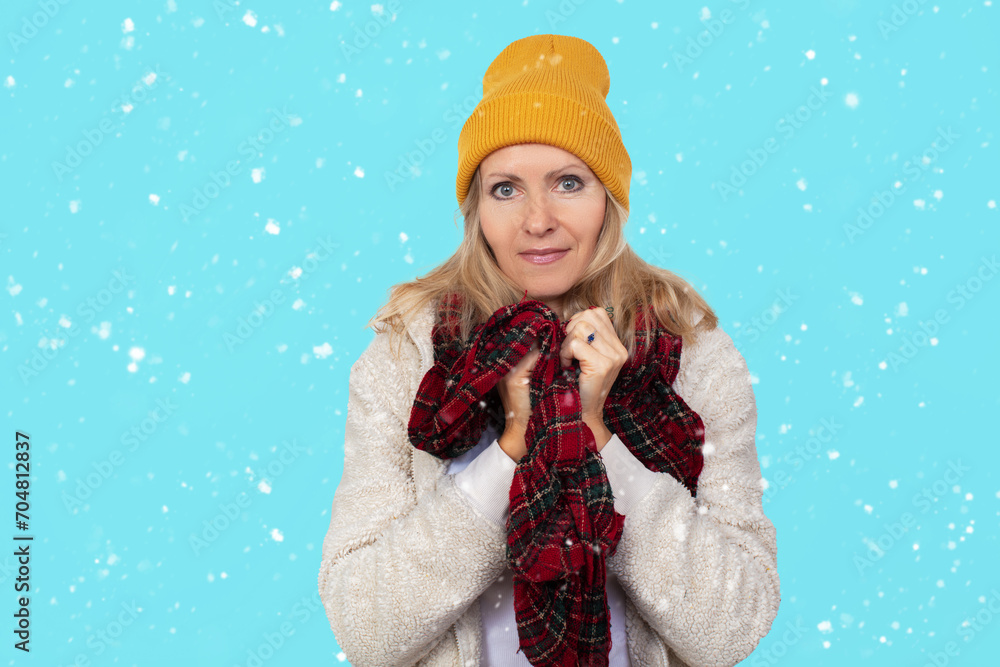 Close-up portrait of an elderly woman in a knitted hat, wrapped in a scarf against the cold on a blue background Close-up portrait of an elderly woman in a knitted hat, wrapped in a scarf against the cold on a blue background
