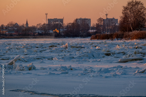 Winter landscape with frozen river with ice drifts and houses at sunset. Landscape with golden sunset light in cold winter evening in Latvia. Jelgava town. photo