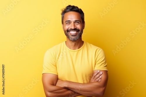 Portrait of a happy Indian man with arms crossed over yellow background