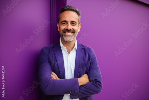 Portrait of a smiling mature man standing with arms crossed against purple background