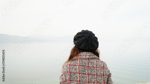 A woman wearing a black hat and tartan scarf is looking out to Lake Ohrid in a foggy scene.
