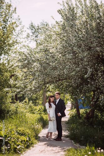 A man and a woman standing on a path in a garden. The woman is wearing a wedding dress and the man is dressed © alenazamotaeva