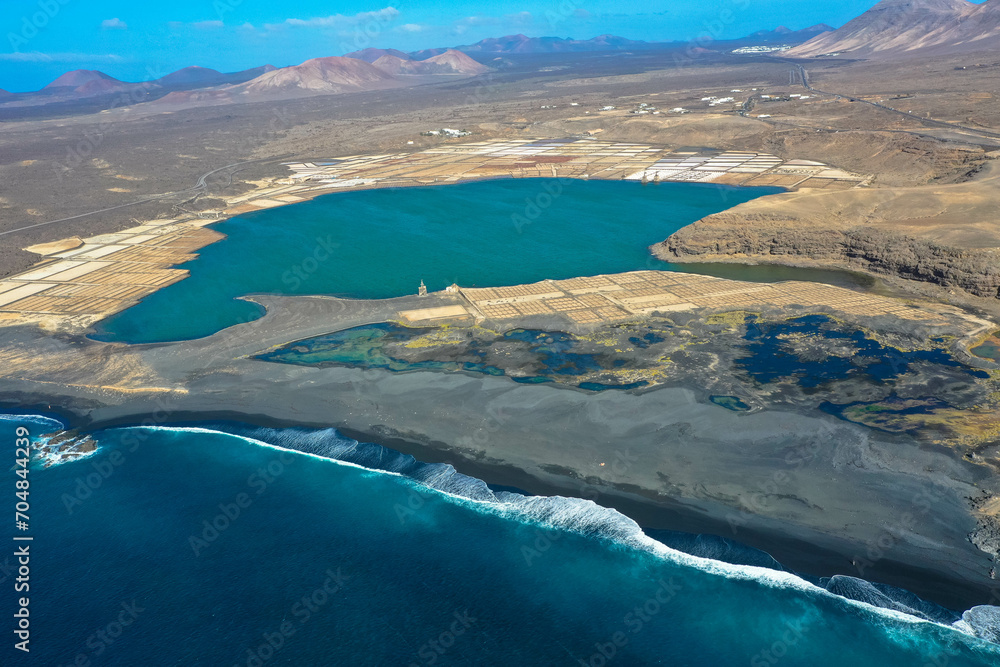 Drone panoramic view of Playa del Janubio in Lanzarote with the volcanic landscape in the background with turquoise sea and big waves. Nature and tourism. Canary Islands, Spain. Drone panoramic view of Playa del Janubio in Lanzarote with the volcanic landscape in the background with turquoise sea and big waves. Nature and tourism. Canary Islands, Spain.