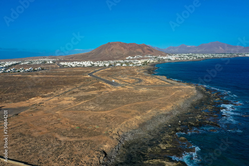Playa Blanca coastline. Aerial drone panoramic view with Red volcano in the Background. Tourism and vacation concept. Flamingo beach Lanzarote, Canary Islands, Spain.