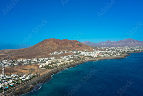 Fototapeta Naklejka Na Ścianę i Meble -  Playa Blanca coastline. Aerial drone panoramic view with Red volcano in the Background. Tourism and vacation concept. Flamingo beach  Lanzarote, Canary Islands, Spain.