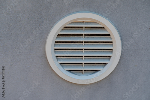 White plastic circular ventilation grill in a gray wall.