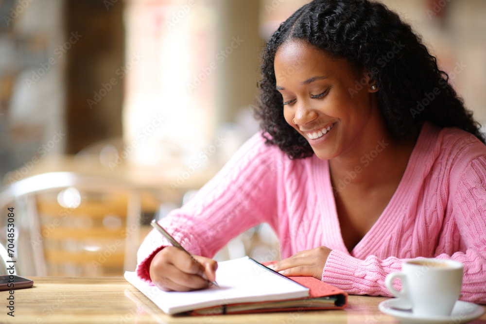 Happy black student taking notes studying in a bar Happy black student taking notes studying in a bar