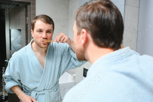 Brushing teeth in the morning. Rear view of handsome young beard man brushing his teeth and smiling while standing against a mirror.