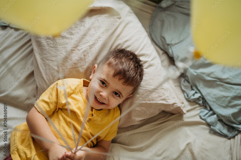 Happy boy holding balloons and lying on bed at home Happy boy holding balloons and lying on bed at home