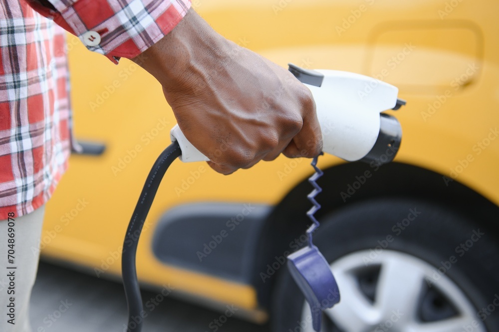 african man holding charge cable in on hand standing near electric car.
