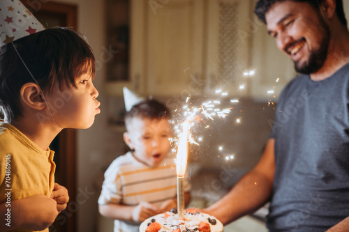Boy wearing party hat and blowing candle on cake with family photo