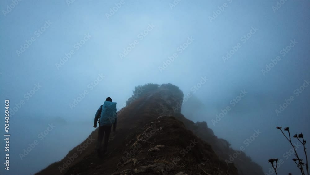 Hiker man with a big backpack hiking on the pick of the mountain on a foggy evening Hiker man with a big backpack hiking on the pick of the mountain on a foggy evening