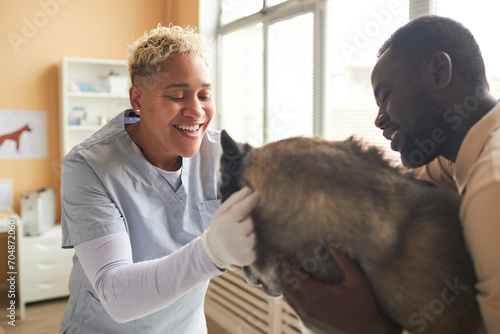 Happy veterinarian petting dog with owner in clinic