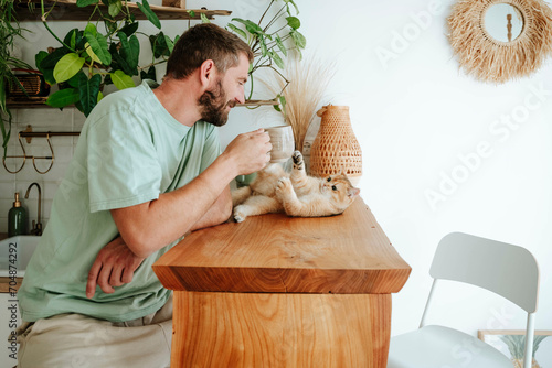 Man playing with cat on wooden table at home photo