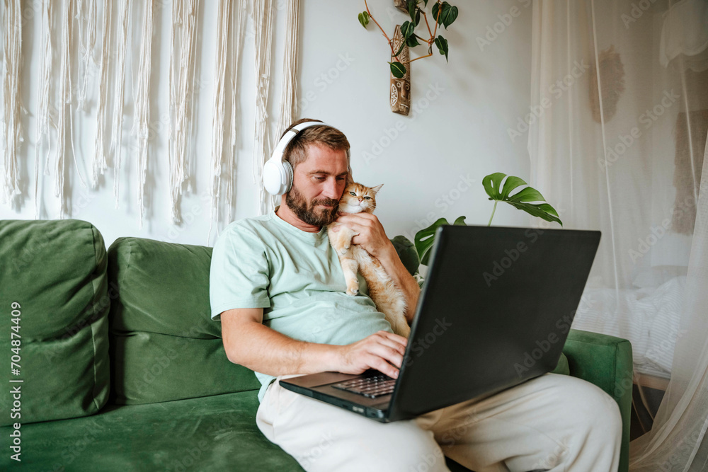 Man with cat sitting on the couch at home and using laptop Man with cat sitting on the couch at home and using laptop