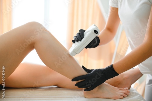 Beautician waxing female legs in spa center photo